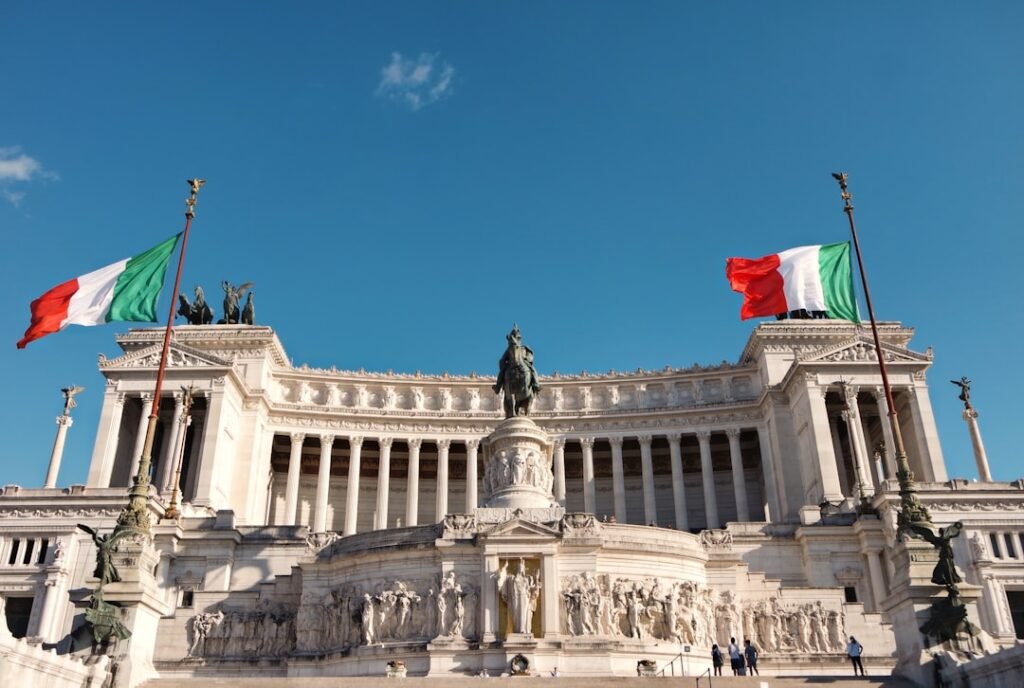 Vista del monumento del Vittoriano en Roma con la bandera de Italia de fondo, representando las herramientas y recursos para la vida en el país.