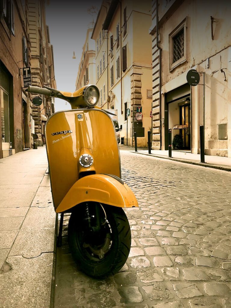 Vespa amarilla clásica aparcada en una calle histórica para alquilar una moto en Italia.