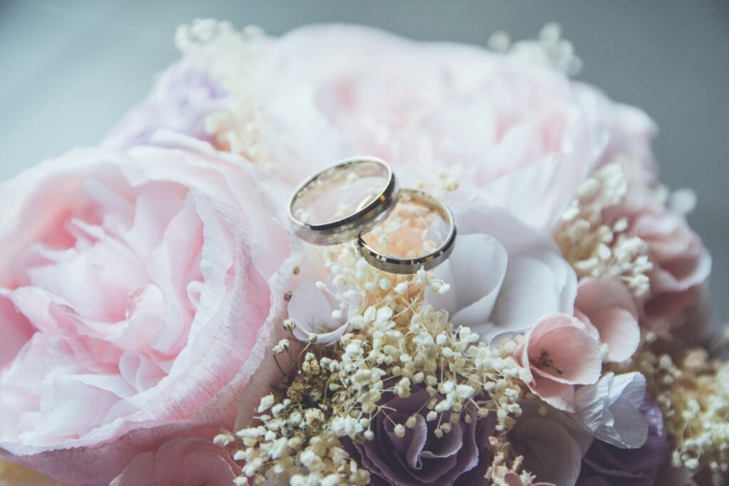 Anillos de boda plateados descansando sobre un ramo de flores rosadas y blancas para la solicitud de ciudadanía italiana por matrimonio.